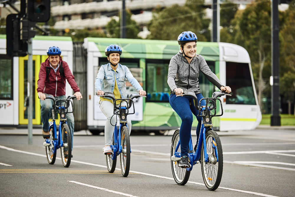 Family cycling using Melbourne Bike Share bikes with tram nearby