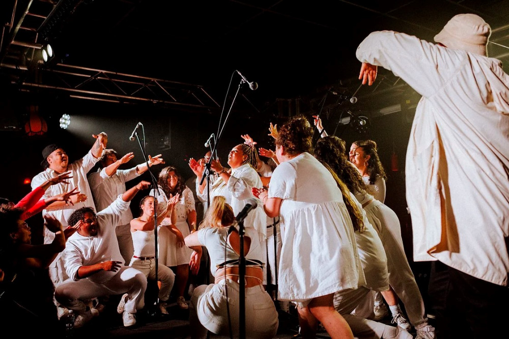 Choir of people dressed in white singing into microphones
