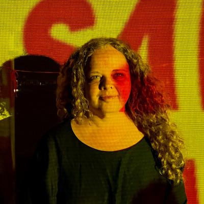 Portrait image of Kait James, with yellow light projected onto her face.