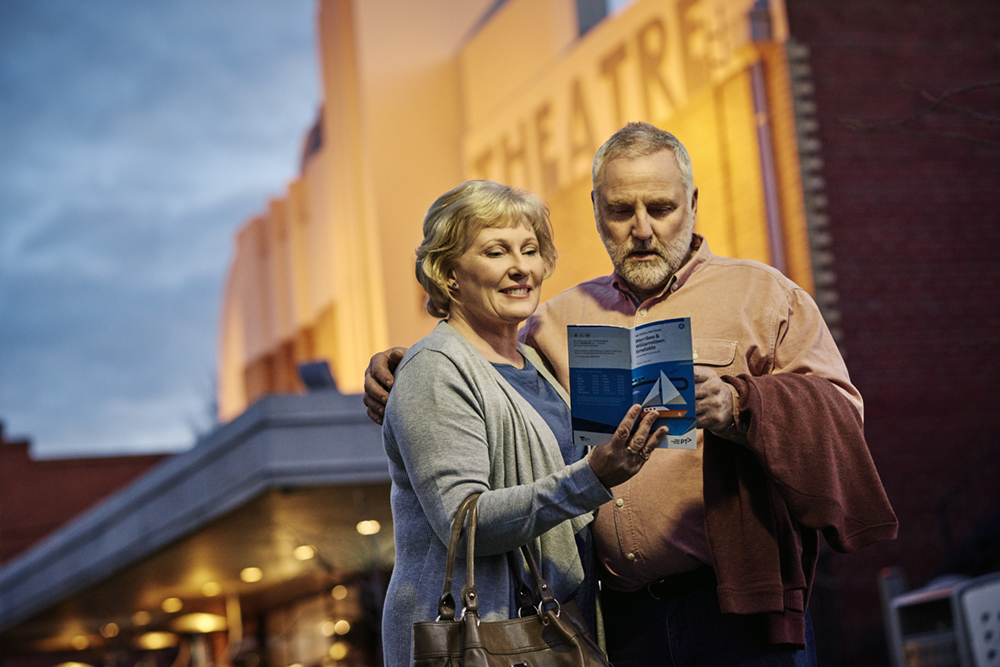 Senior couple reading travel brochure outside Sun Theatre