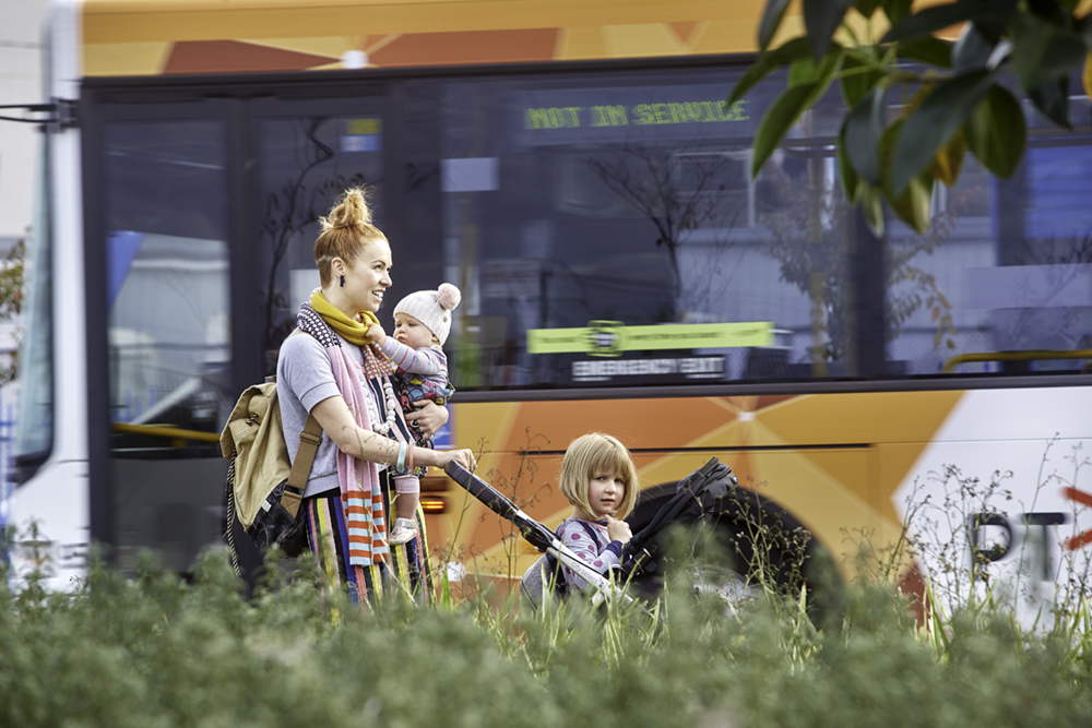 Bus travelling near mother with pram and baby 