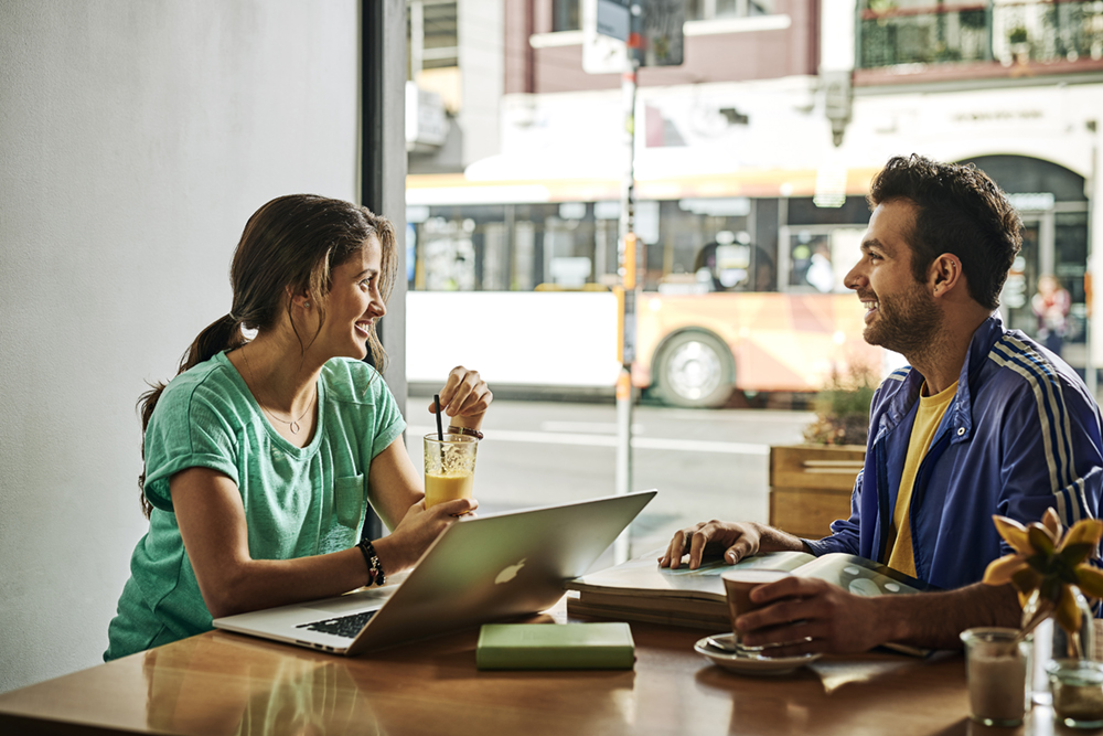 Young people in cafe using laptop with bus in background